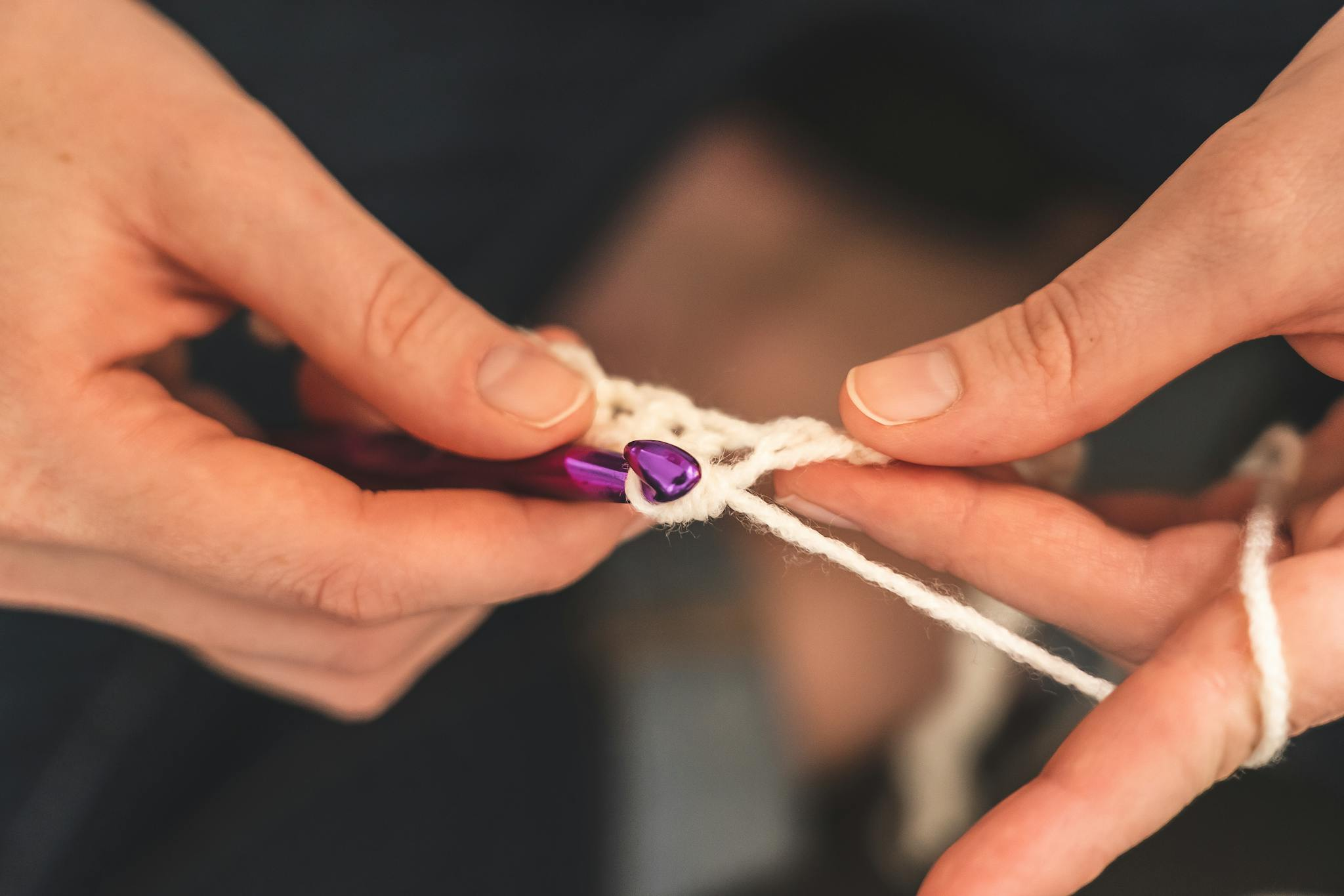 Detailed view of hands skillfully crocheting with a purple hook, featuring soft yarn and intricate craftsmanship.
